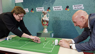 Bundesministerin Klara Geywitz und Staatssekretär Dr. Rolf Bösinger spielen Tipp-Kick. Im Hintergrund der EM-Pokal
