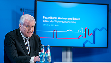 Bundesinnenminister Seehofer vor einerm Bildschirm mit der Aufschrift "Wohnraumoffensive"
