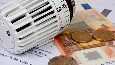 Auf einer Heizkostenabrechnung liegt Geld und ein Heizkörperthermostat