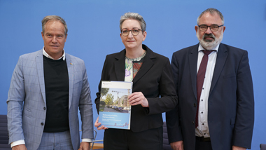 Bundesministerin Klara Geywitz zusammen mit Herrn Eltges (BBSR) und Herrn Prof. Dr. Würzner in der Bundespressekonferenz. Frau Geywitz hält die Studie in der Hand und präsentiert sie den Medienvertretern.