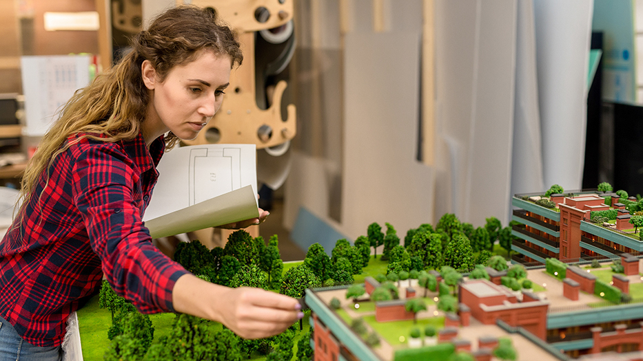Eine junge Frau mit einem Bauplan in der Hand setzt Bäume in einem Stadtentwicklungsmodell