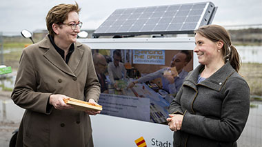Ministerin Geywitz im Gespräch mit einer Frau vor einer solarbetriebenen Projekttafel.