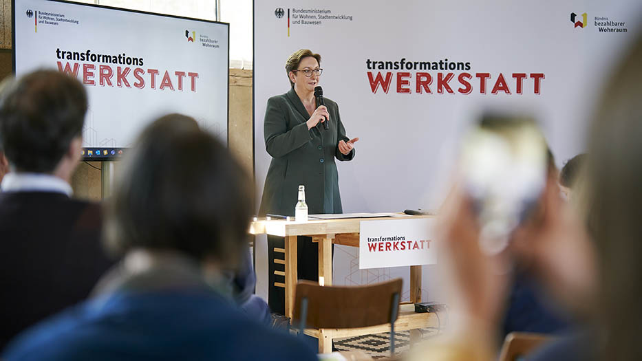 Bundesministerin Klara Geywitz steht mit einem Mikrofon in der Hand vor den Teilnehmerinnen und Teilnehmern der Transformationswerkstatt